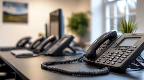 Modern office desk with multiple black office phones potted plant computer monitor background